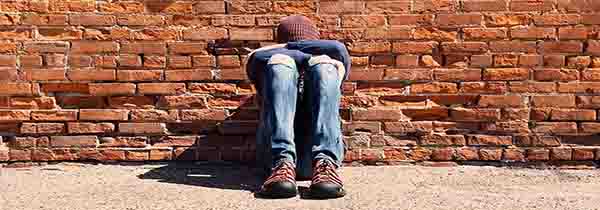 An unhappy man sitting against brick wall