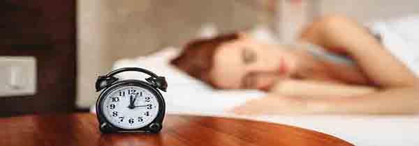 alarm clock next to woman sleeping in bed