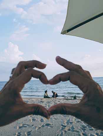 couple on the beach seen through heartshaped hands